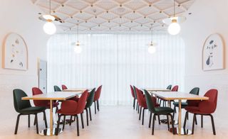 A hotel meeting area with four wooden tables with four chairs at each, wall paintings, a patterned ceiling and round pendant lights.