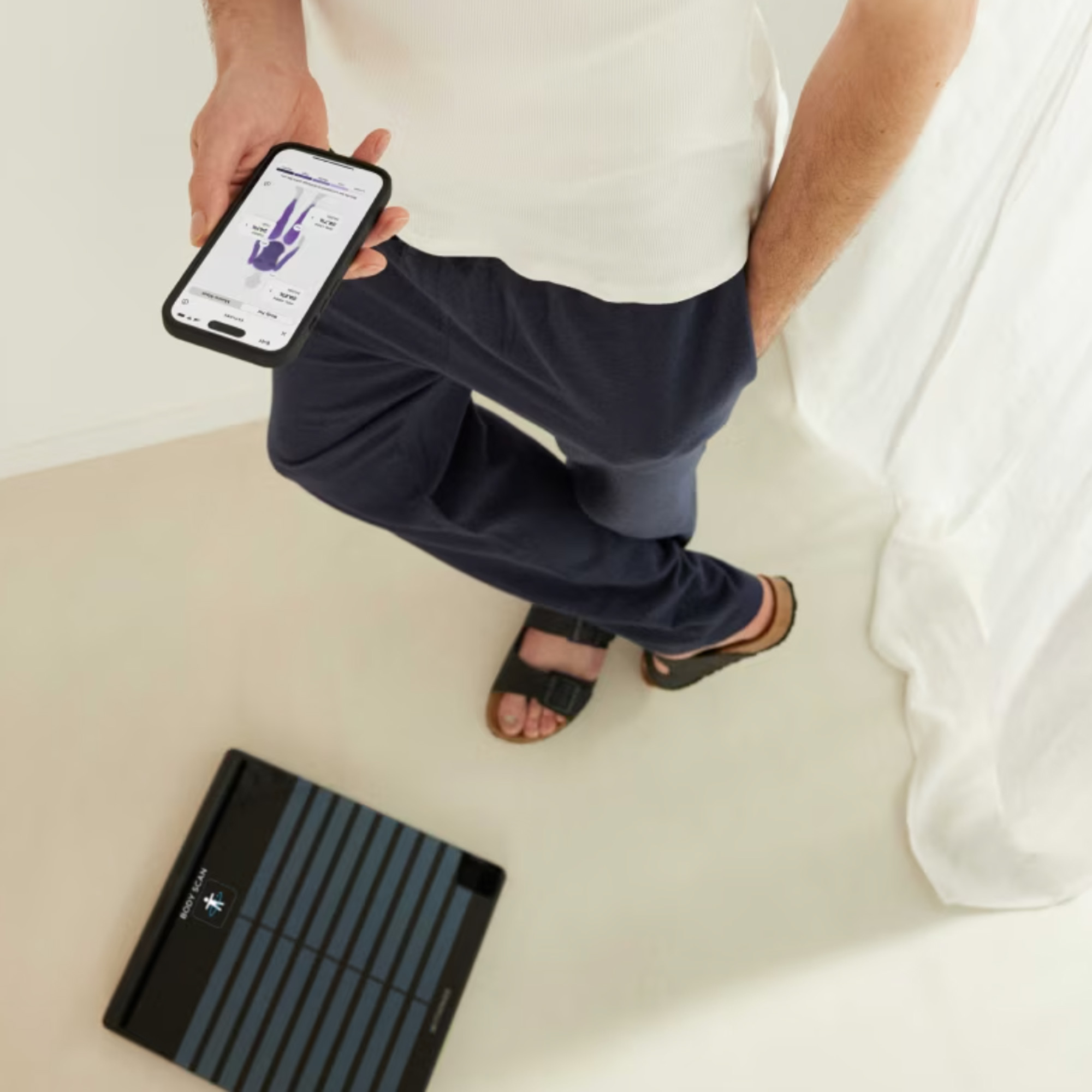a man standing beside a Withings smart scales with a companion app open on his smartphone