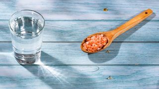 Glass of water on a bench with a spoon full of Himalayan salt next to it