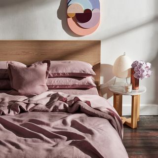 A wooden bed dressed with pale pink linen bedlinen and a sculptural artwork on the wall