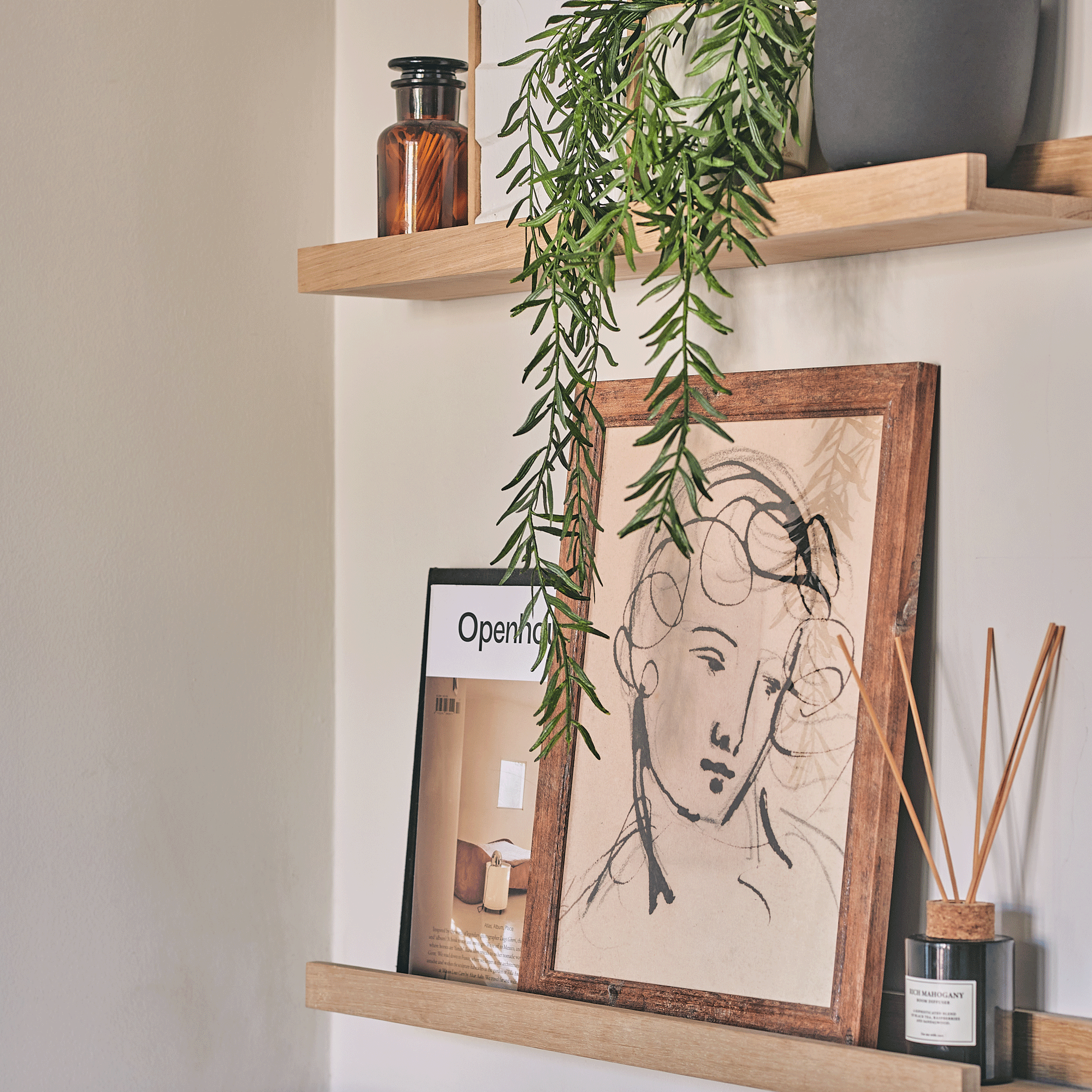 a set of wall shelves with various items on display including a trailing houseplant, a framed print and a reed diffuser