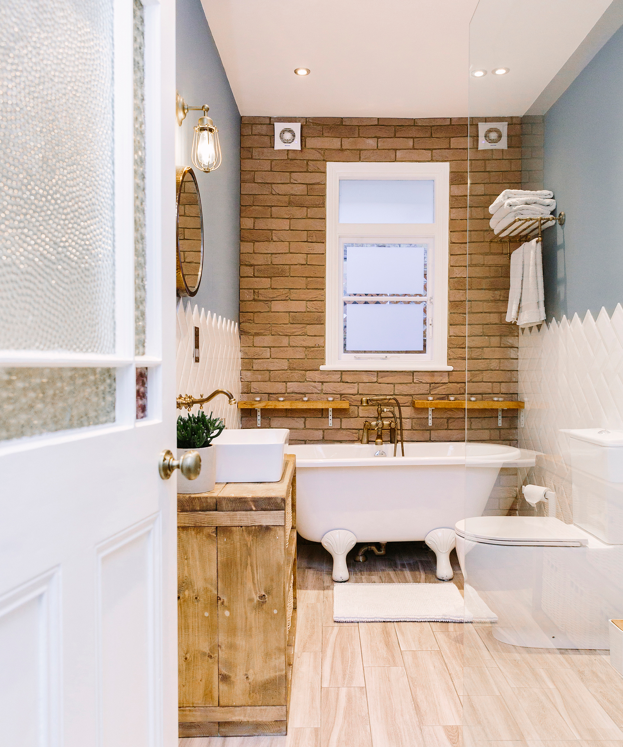 An example of small bathroom ideas showing a bathroom with a vinyl wood floor, brick wall with tiles and paint opposite and a small freestanding tub