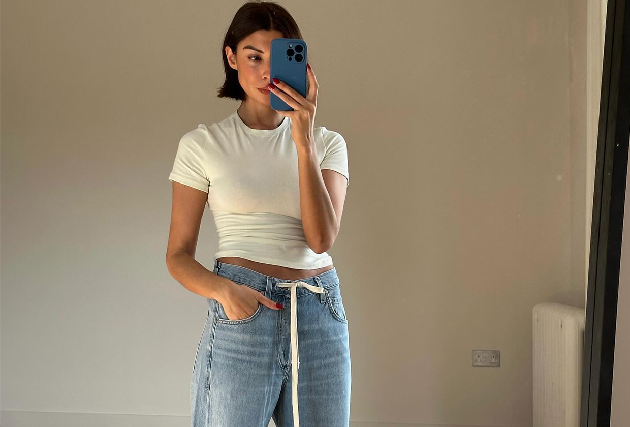 Woman taking a mirror selfie wearing a white tee and jeans.