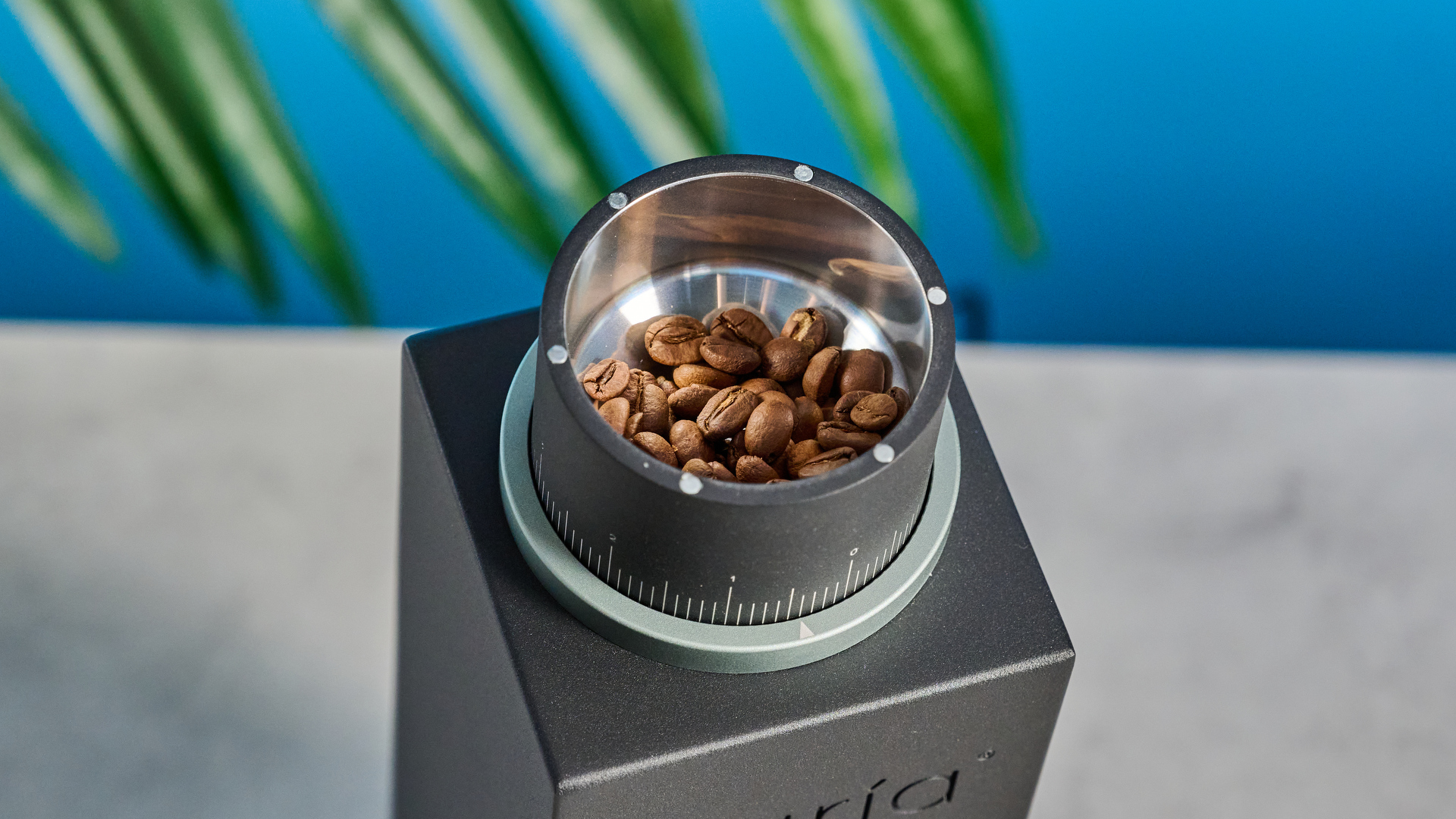 The Varia VS3 coffee grinder in use on a stone surface with a blue background