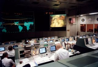 On April 13, 1970, Eugene F. Kranz, one of four Apollo 13 flight directors, communicates with Apollo 13 lunar module pilot Fred Haise in the fourth television transmission from the Apollo 13 mission. Kranz sits with his back to the camera in the Missions Operations Control Room at the Manned Spacecraft Center.