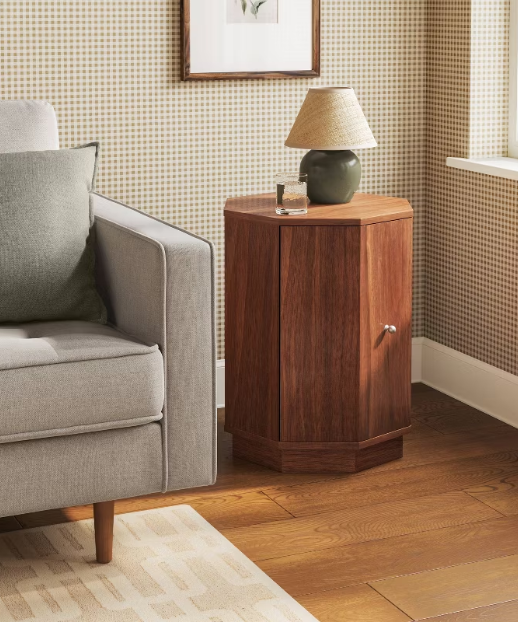 a room with gingham wallpaper, an octagonal side table, a grey couch, and hardwood floors