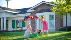 Father balances kid on his legs in the front yard