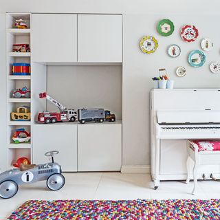 White wall and storage cabinet kids play area with toys and a multi-colorued rug