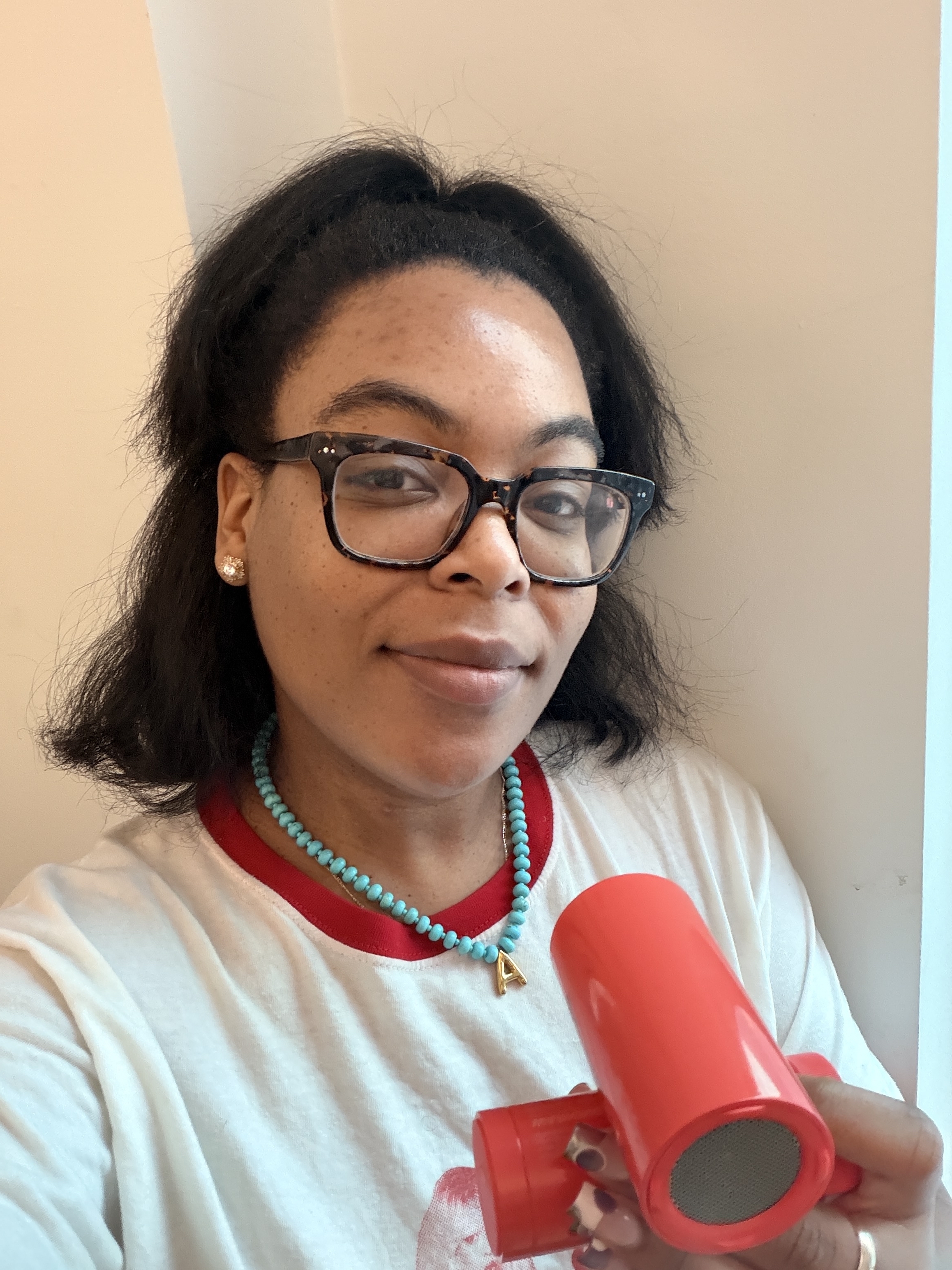 a black woman with dark hair in a white t-shirt and glasses holding a red personal fan