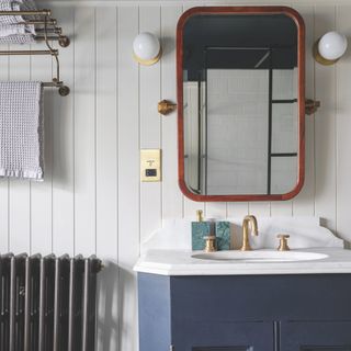 White panelled bathroom with black radiator, blue sink cabinet and a large mirror above