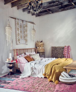 An example of bohemian bedroom ideas showing a rattan bed with white bedding, a yellow throw and a pink rug