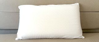 A white Bearaby SoftForm pillow leaning against a grey fabric headboard