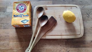 Image shows a wooden chopping board and some wooden utensils next to a lemon and some bicarbonate of soda.
