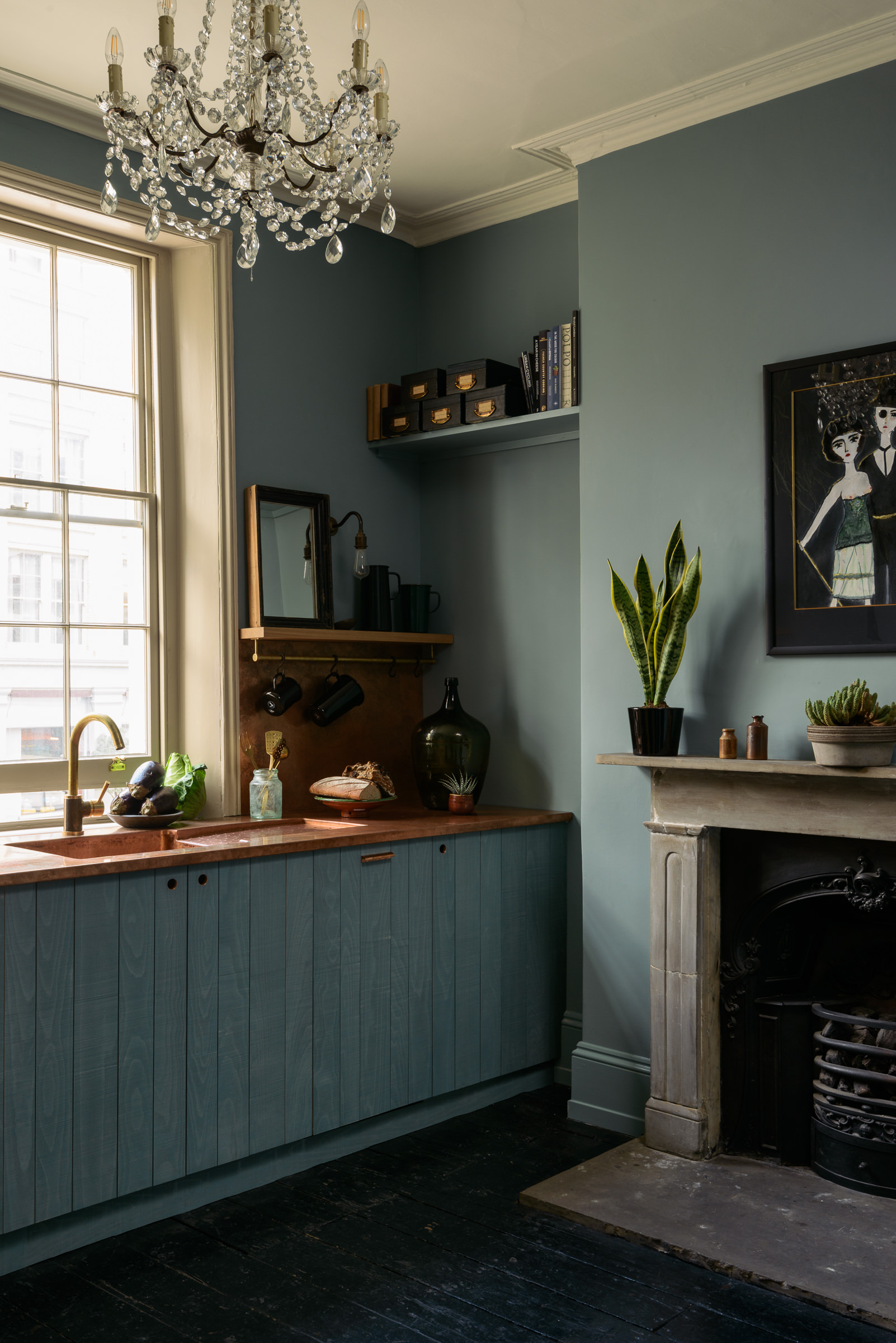 A kitchen painted gray with a fireplace and glass chandelier