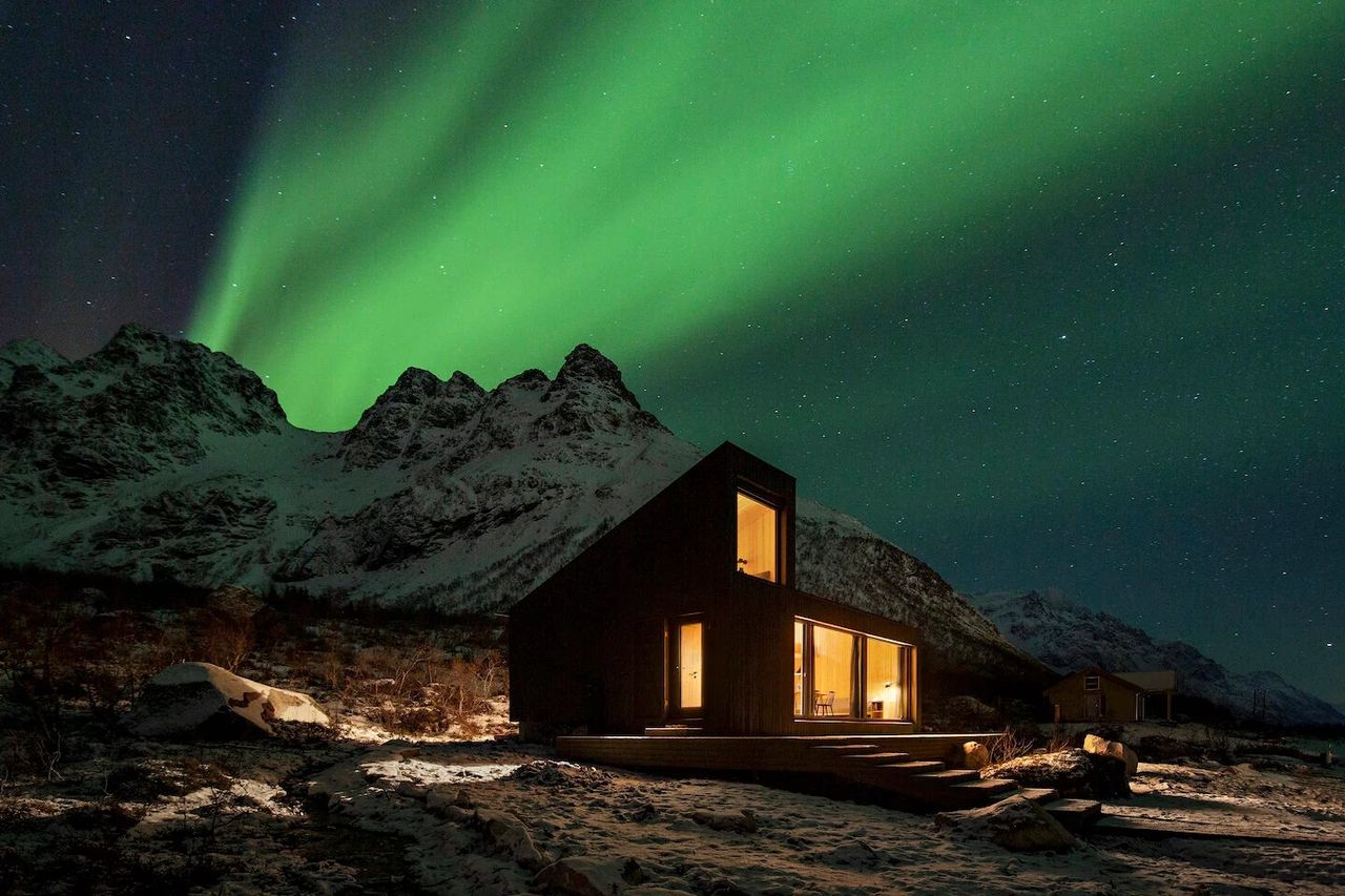 Aurora borealis graces a wooden cabin in the mountains at night.