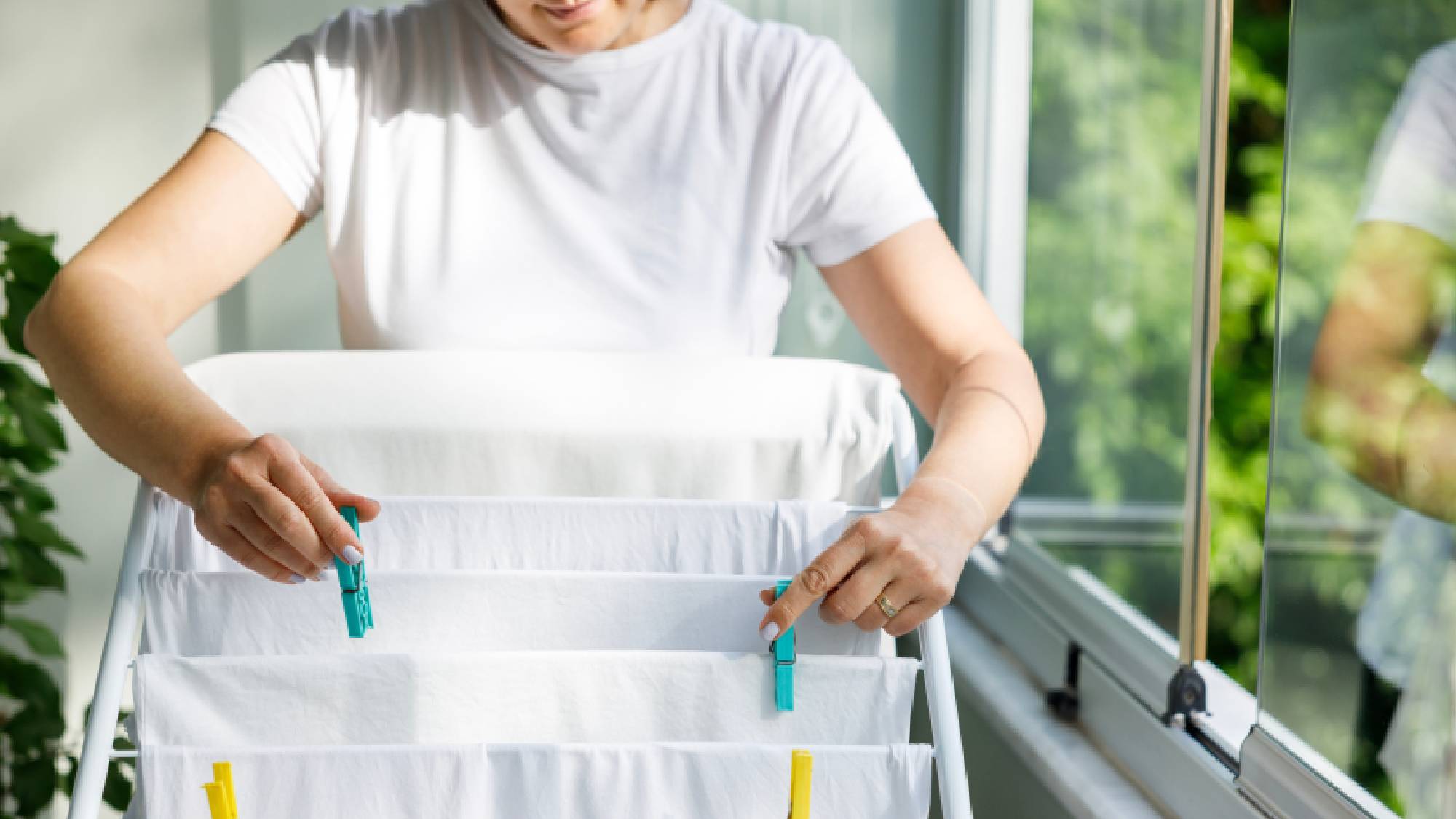 Woman using brightly colored clothes pegs to neatly secure white garments onto an indoor drying rack