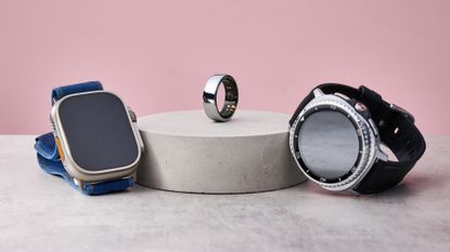 The Apple Watch Ultra 2 and Samsung Galaxy Watch 8 Classic sit either side of a stone podium, on which sits the Oura Ring 3.