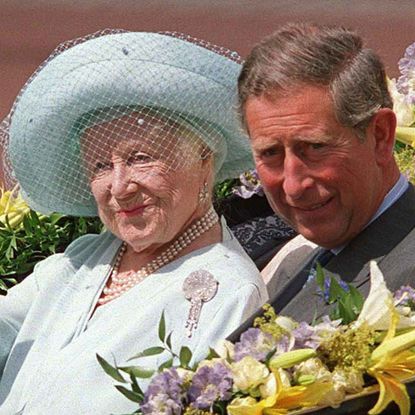 The Queen Mother wearing a blue hat and coat waving from a carriage with King Charles