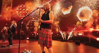 Nigel Tufnel wears a tartan kilt as Spinal Tap perform live with pyro and sparks lighting up the stage.