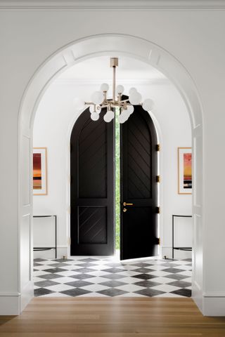 hall with monochrome tiled floor and black arched double front door with modern chandelier above