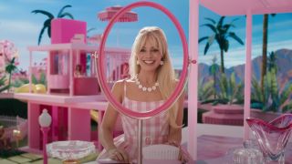Margot Robbie as Barbie looking into a bright pink mirror.