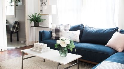 White coffee table with fresh roses and neutral ornaments staged in front of large blue sectional couch 