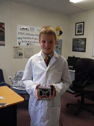 A student from St. Thomas More Cathedral School holds the STMSat-1 cubesat.