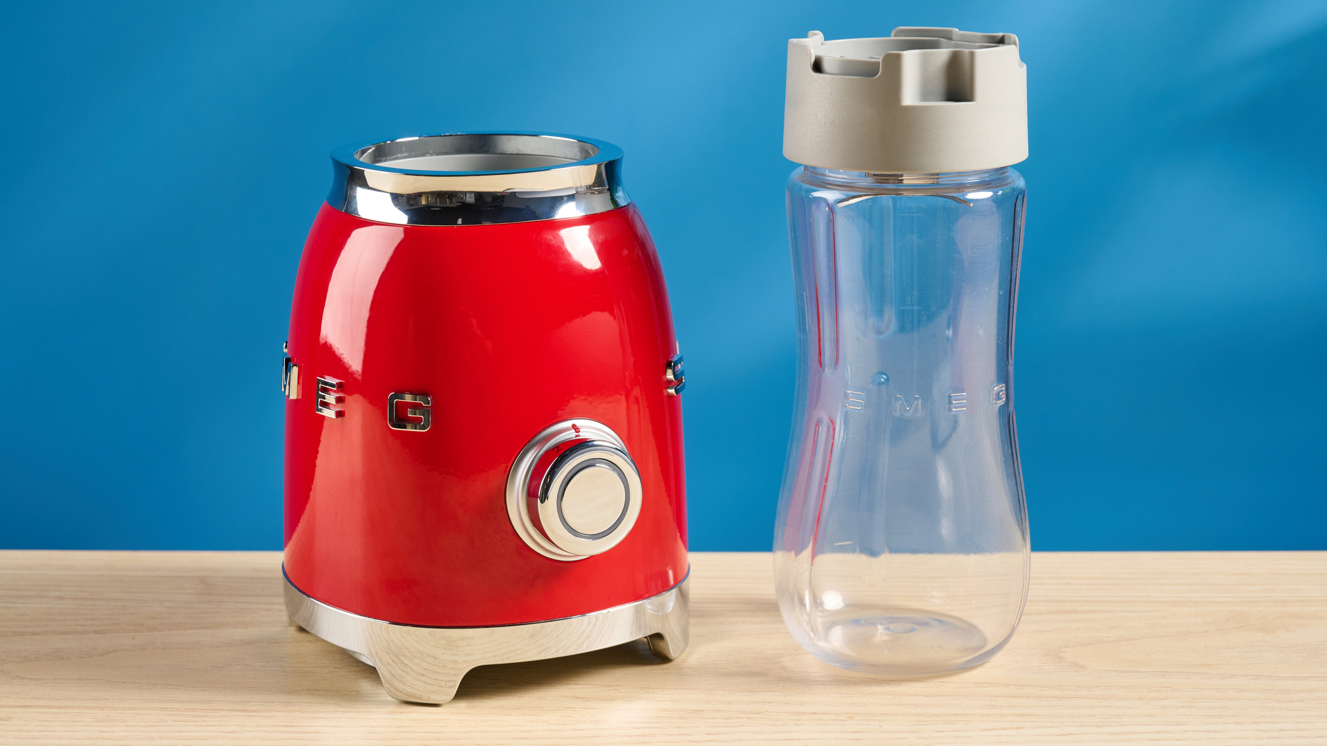 Smeg Personal Blender in the red colorways photographed in front of a blue background.