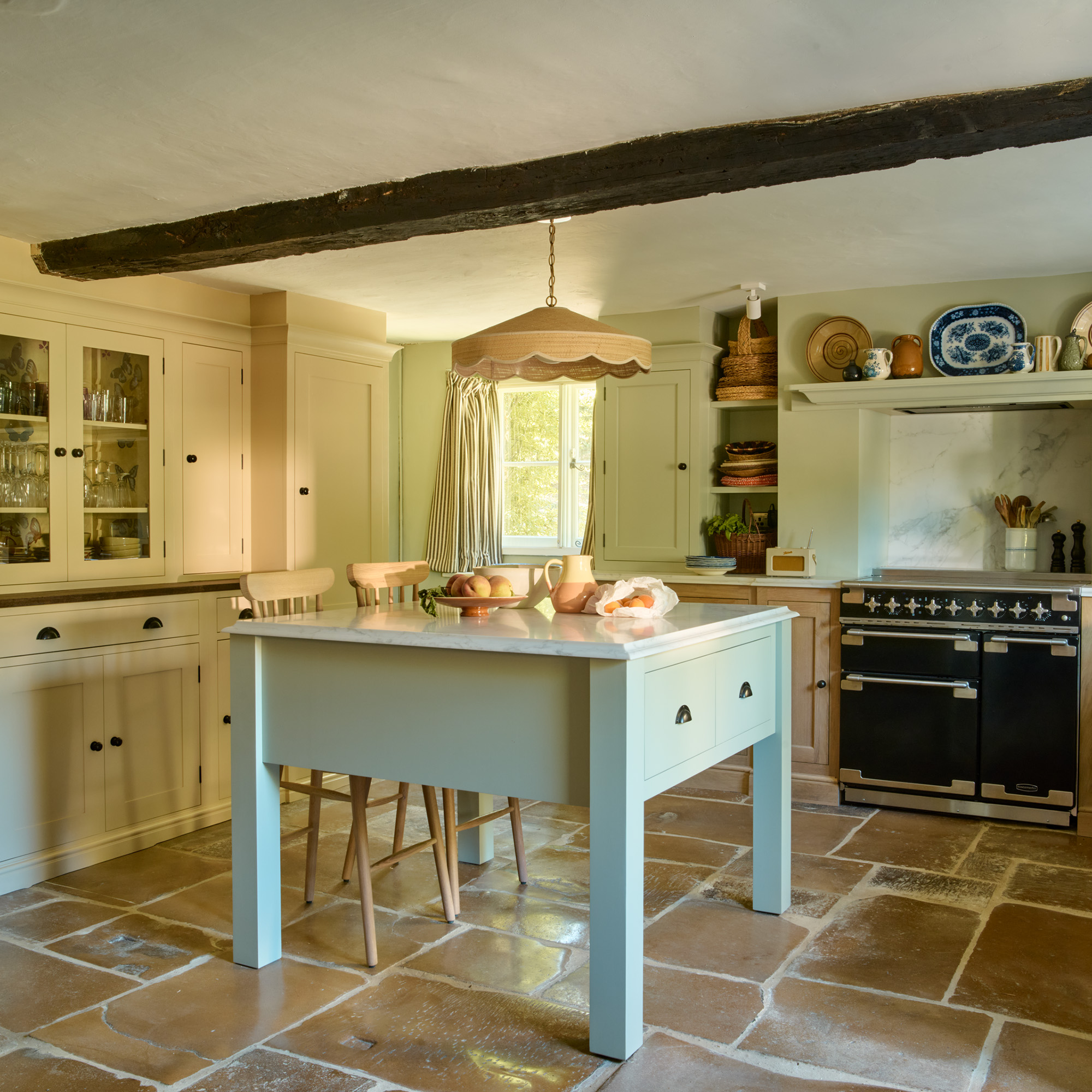 small sage kitchen island in a country kitchen with beamed ceiling, flagstone floor and black range cooker