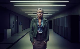The Teacher - Sheridan Smith as Jenna, standing in a school corridor wearing a silk shirt, tweed skirt, leather jacket and staff ID laminate, with a worried look on her face