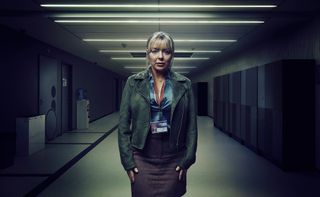 Sheridan Smith as Jenna, standing in a school corridor wearing a silk shirt, tweed skirt, leather jacket and staff ID laminate, with a worried look on her face