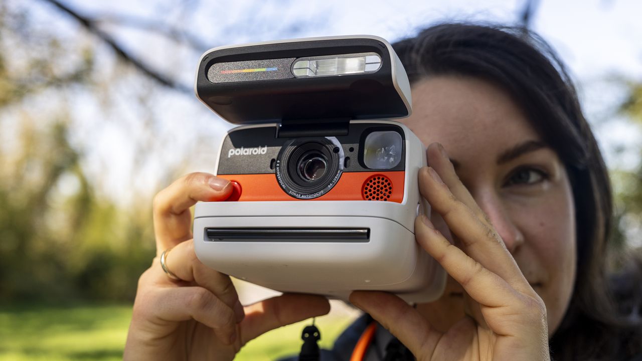 A female photographer holds the Polaroid Flip instant camera in a sunny field