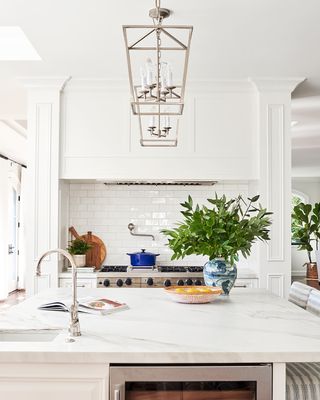 close up of island in white open plan kitchen with pendant lights, chrome taps and flowers in a vase