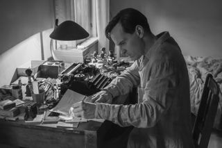 a man (andrew scott as tom ripley) writes at a desk filled with forging supplies and a typewriter, in netflix's 'ripley'