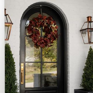 A black arched front door with a dark red-purple seasonal wreath