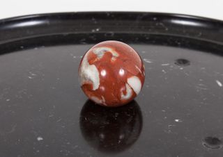 Red and white marble ball on a black marble surface photographed against a grey background