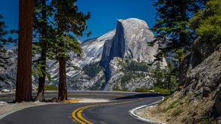 A winding road in Yosemite showing Half Dome in the distance