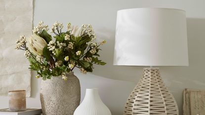 A large jar of spring time flowers next to a lamp against a cream wall