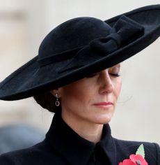 Kate Middleton wearing a black coat and hat closing her eyes