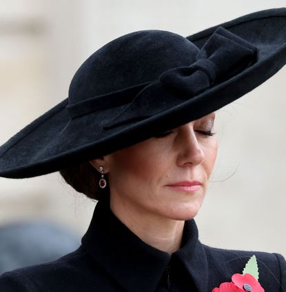 Kate Middleton wearing a black coat and hat closing her eyes