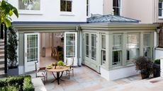 an elegant gray and white orangery addition to a period home by Westbury, with a dining table seen through the open doors and a dining set on the patio