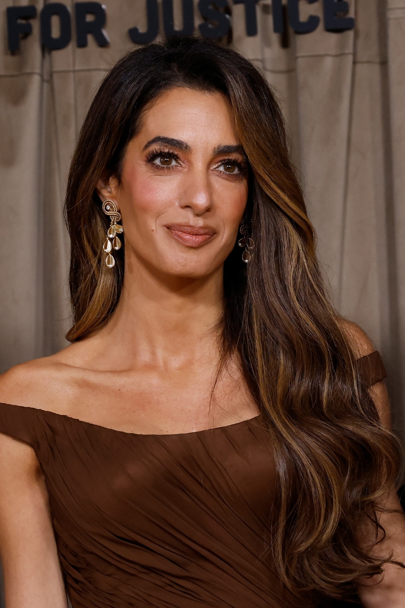 Amal Clooney is picture with long, glossy hair and wearing a brown dress at the Clooney Foundation For Justice's The Albies at The Natural History Museum on October 03, 2025 in London, England.