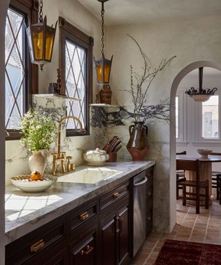 A kitchen with brown cabinets, marble countertops, and brass hardware