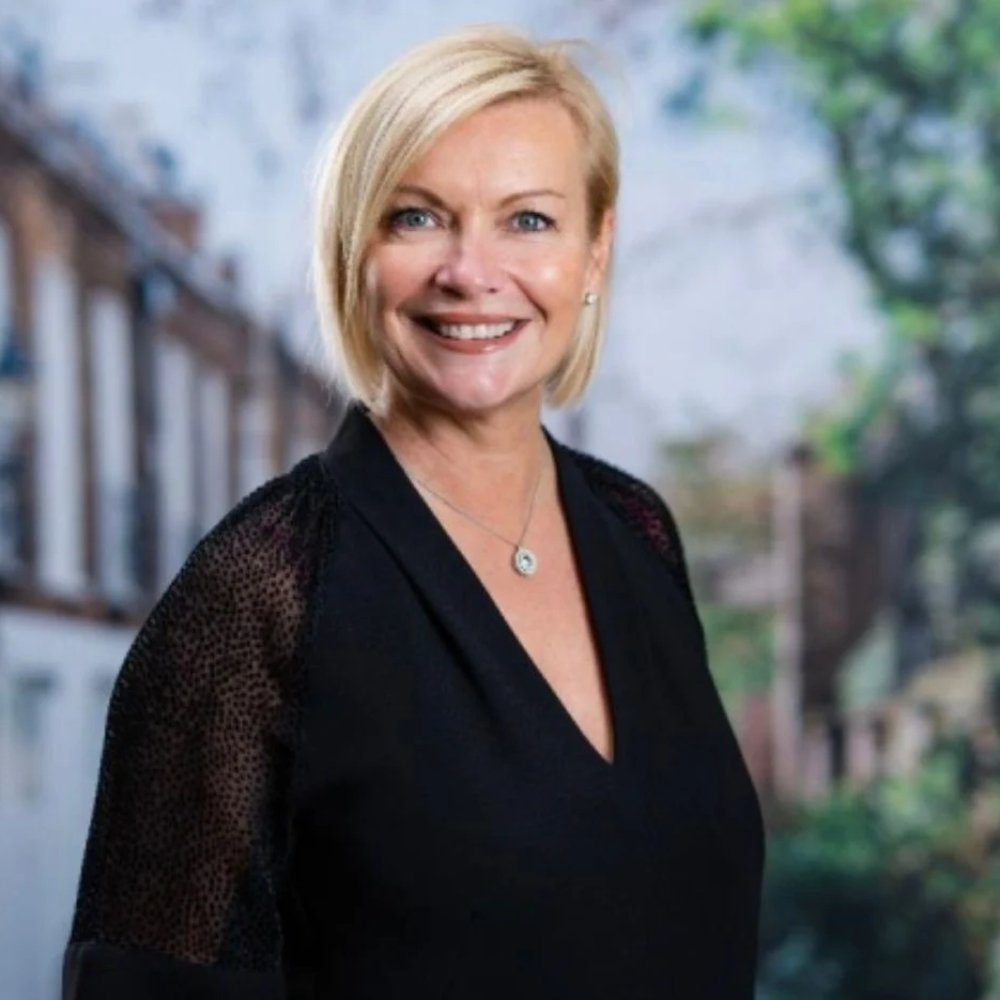 female with short blond bob wearing black blouse stood against backdrop of a street