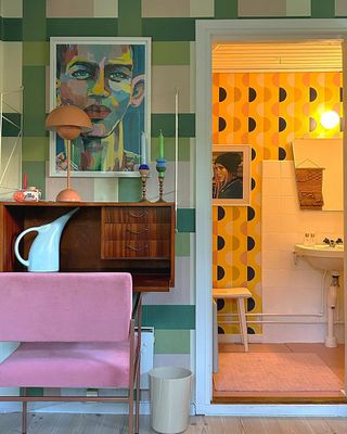 A colorful room with a console table, seat, and bathroom in the background