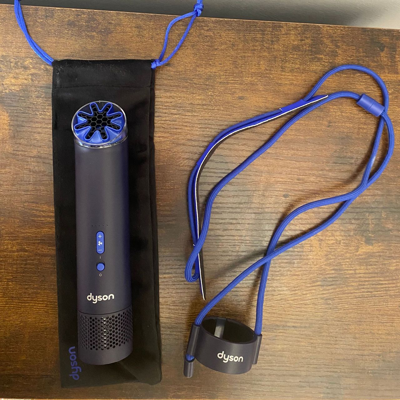 Dyson HushJet Mini Cool Fan rested on the travel pouch next to the neck dock on a wooden surface