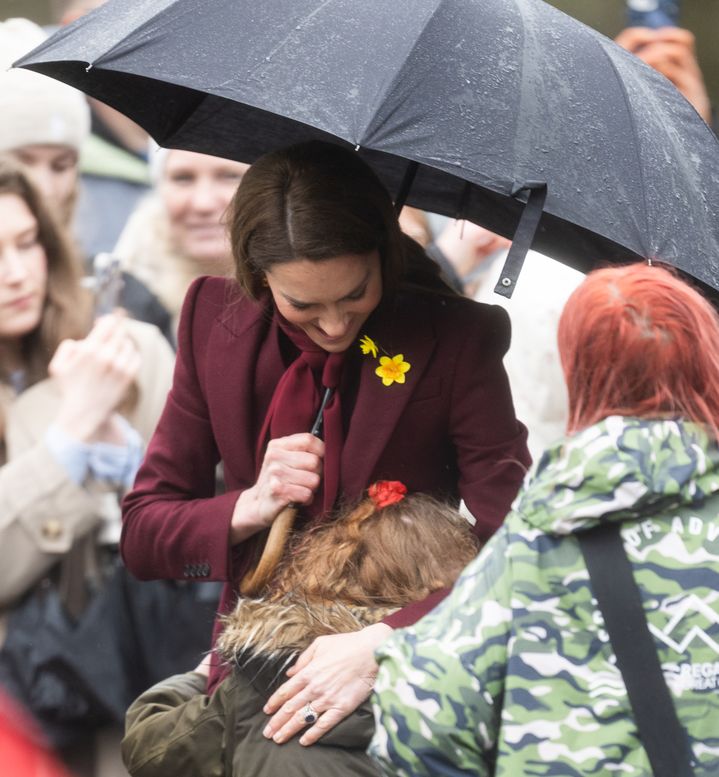 Princess Kate hugging a little girl and holding an umbrella