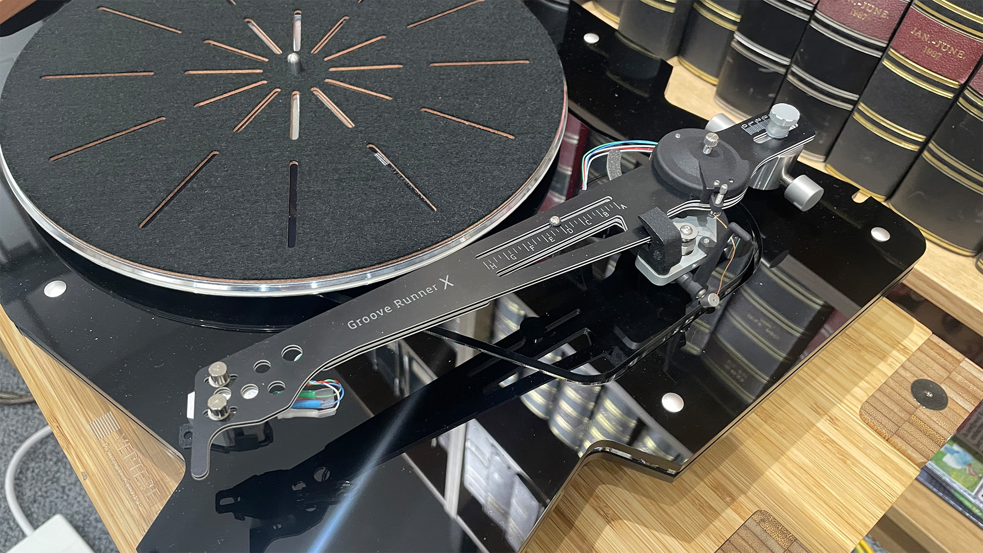 Vertere DG-X turntable on wooden hi-fi rack in front of bookcase detail of tonearm and platter