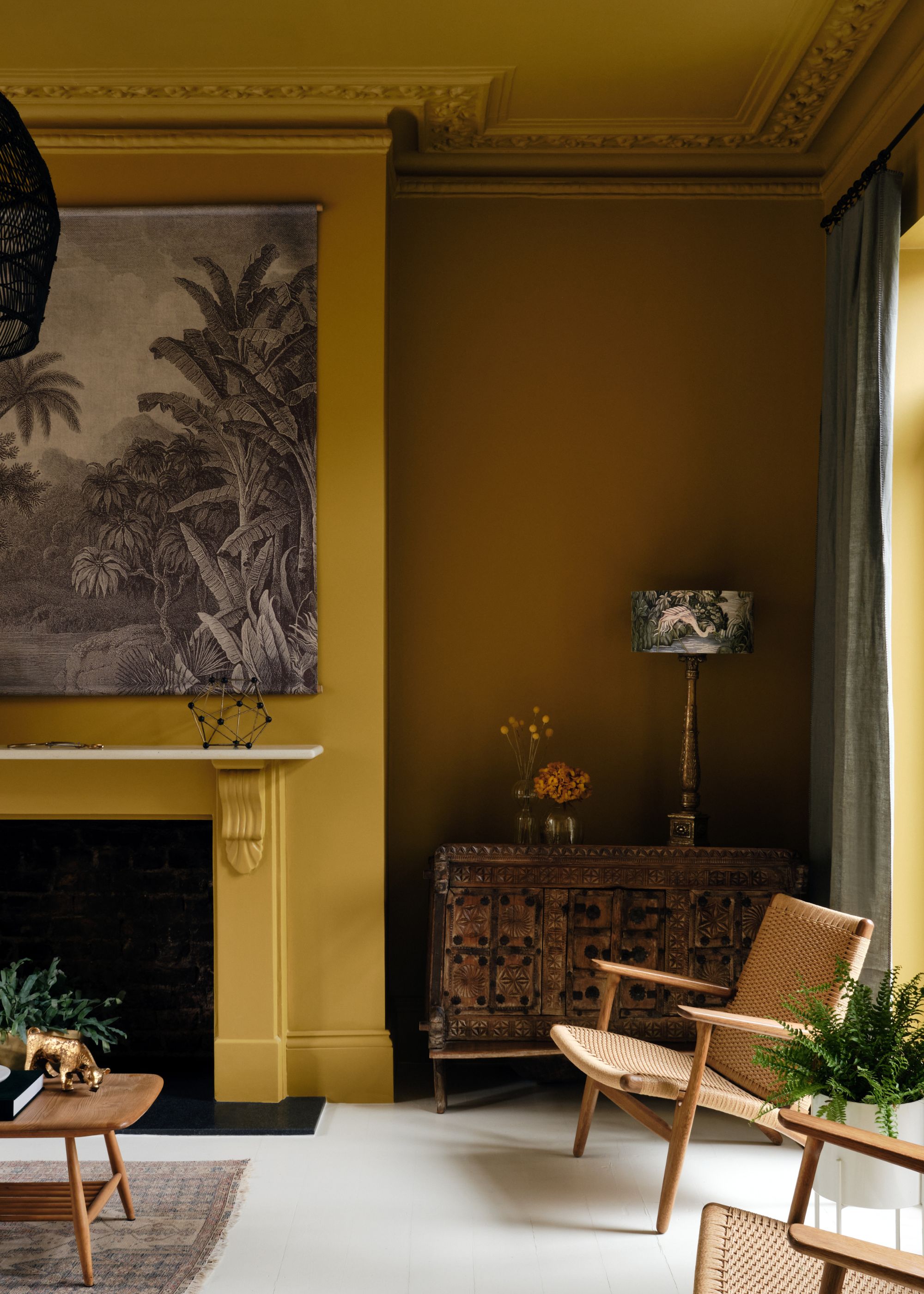 A large, traditional living room with dark ochre walls and a fireplace, and a large piece of artwork above it.