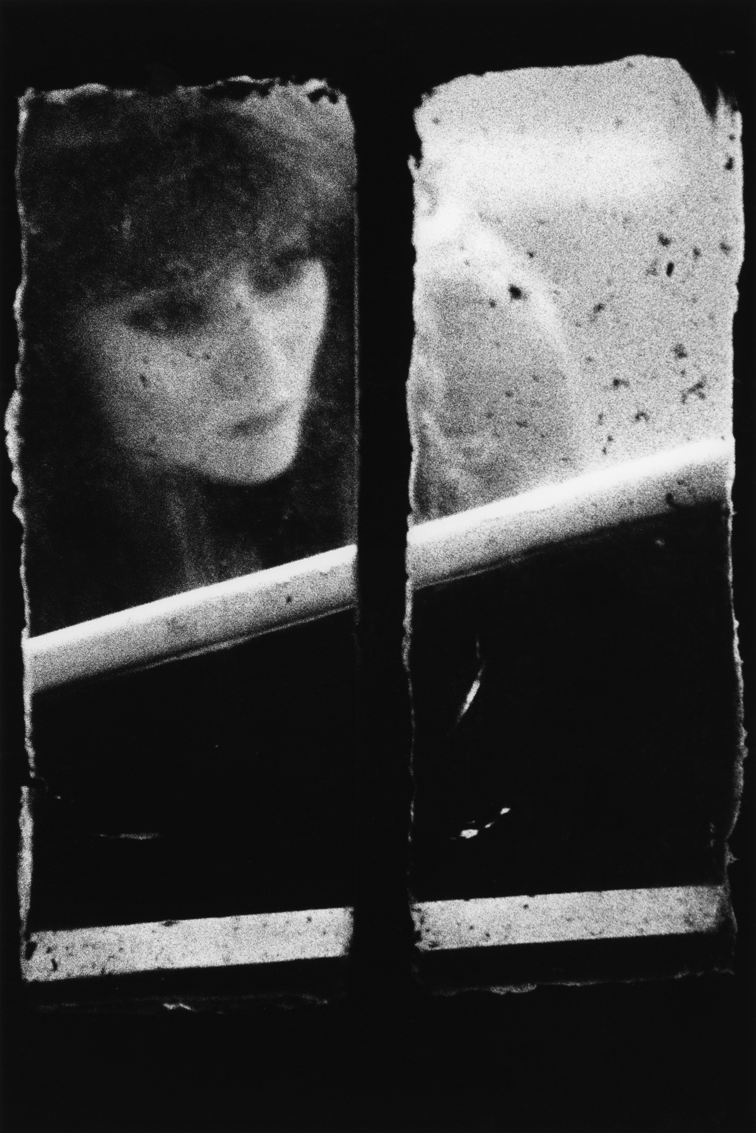 A woman's face is dimly visible through a grimy, cracked window pane divided by a metal bar, the glass speckled with dirt and condensation.